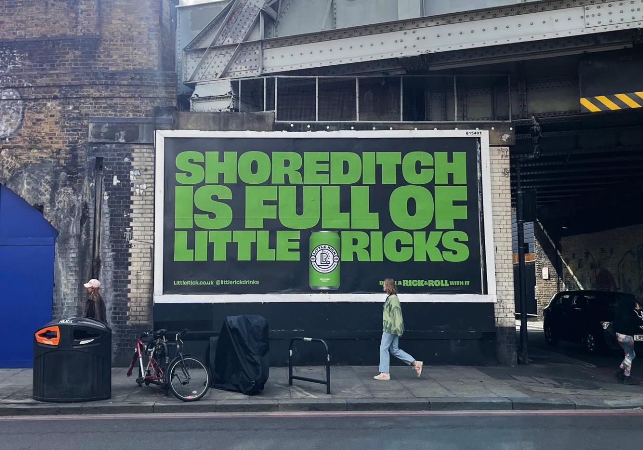 Large green billboard reads Shoreditch is full of little Ricks on a brick wall by the street.